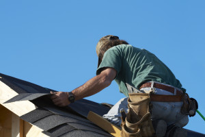 worker on roof putting shingles down